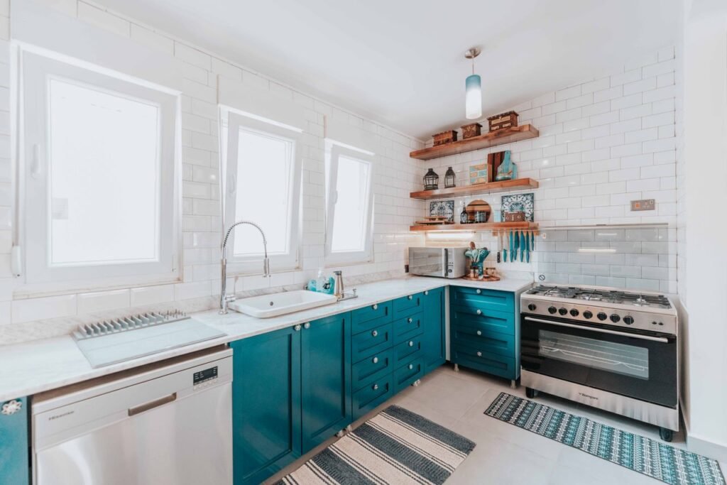 Bright modern kitchen featuring blue cabinets, open wooden shelves, and stainless steel appliances.