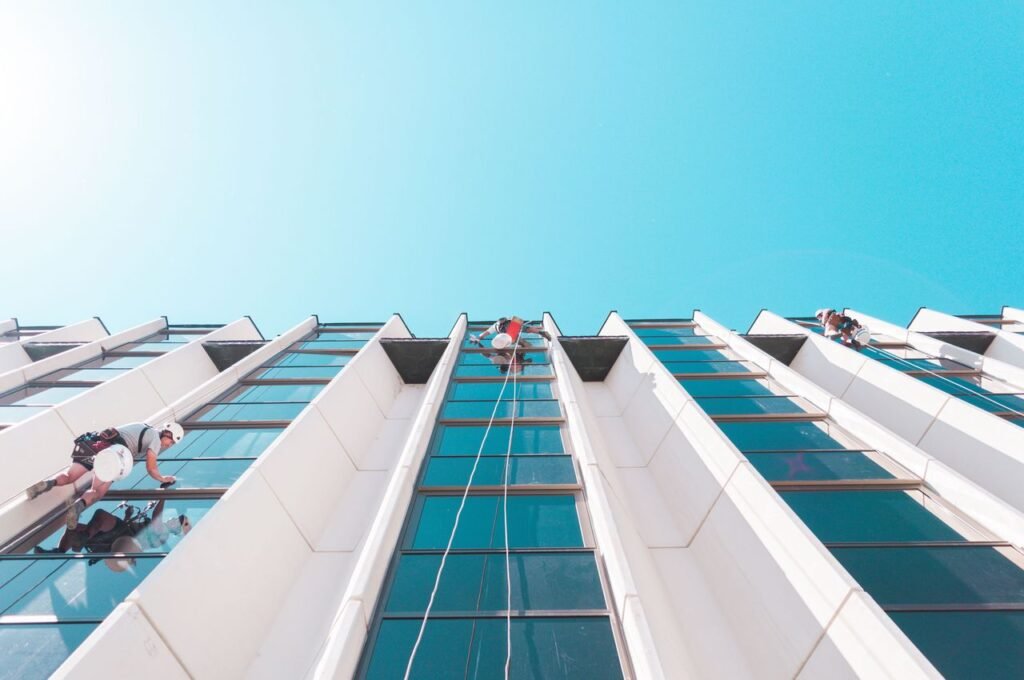 A team of workers cleaning skyscraper windows in Budapest under a clear blue sky.
