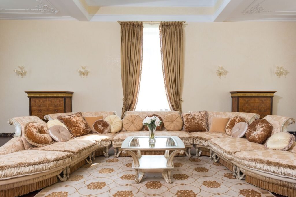 Interior of comfortable spacious living room with soft pillows on long couch and glass table with vase filled with flowers